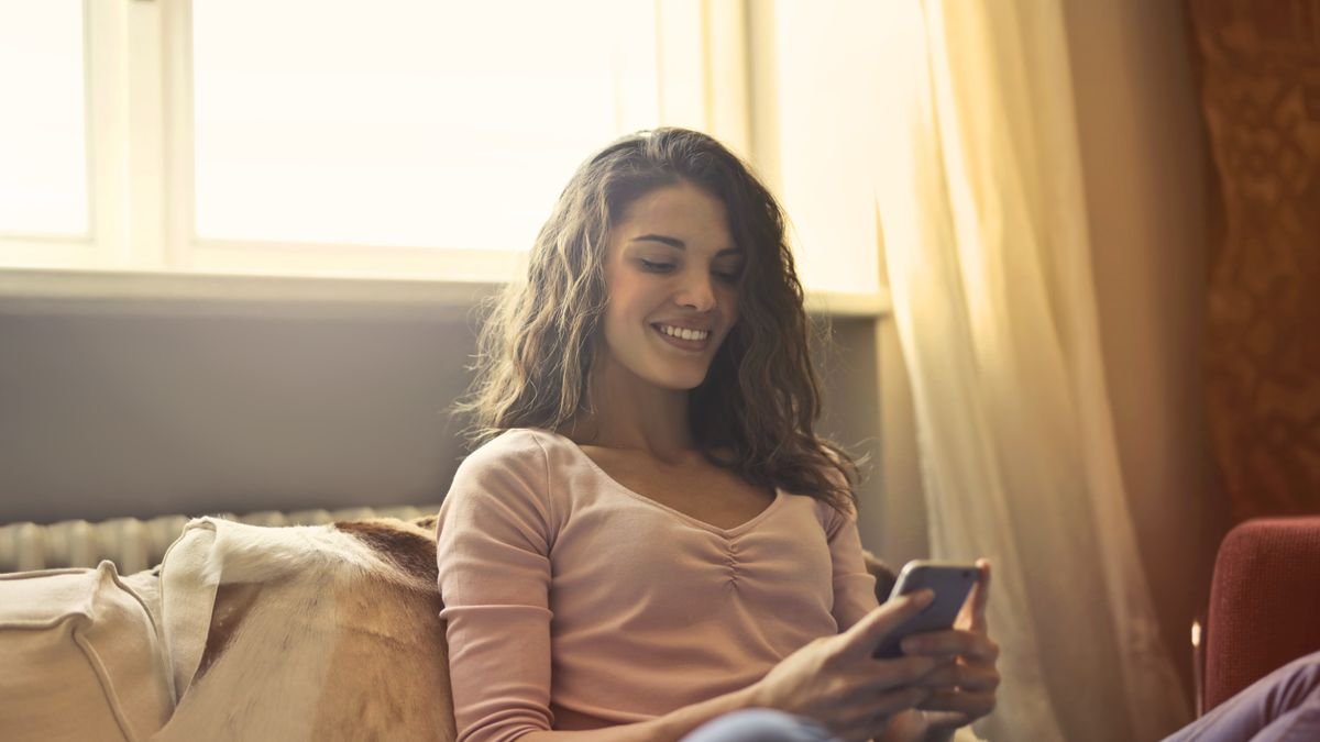 Smiling woman answering a survey on her smartphone at home