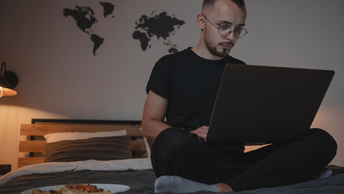Man sitting on his bed with a laptop, working remotely