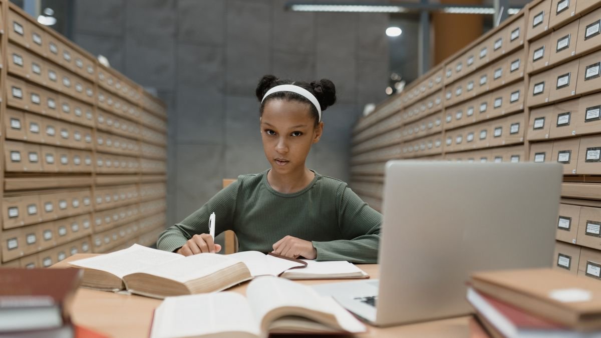 Student studying at a library desk with books and a laptop