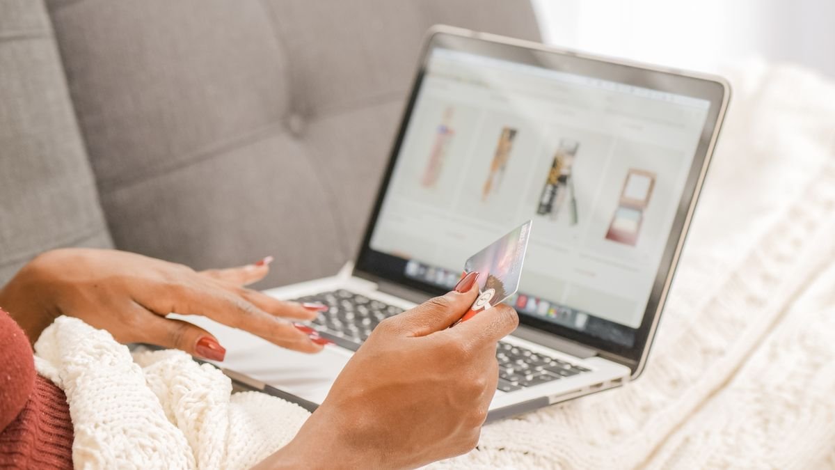Woman on a couch shopping online with a laptop and a card