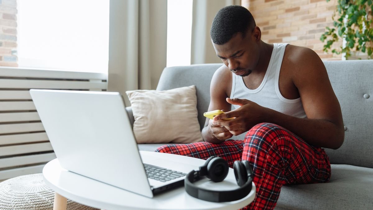 Man on a sofa using a laptop and a smartphone in his spare time