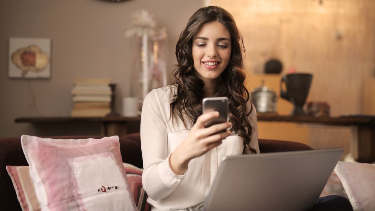 Woman using a smartphone and a laptop in a cosy living room